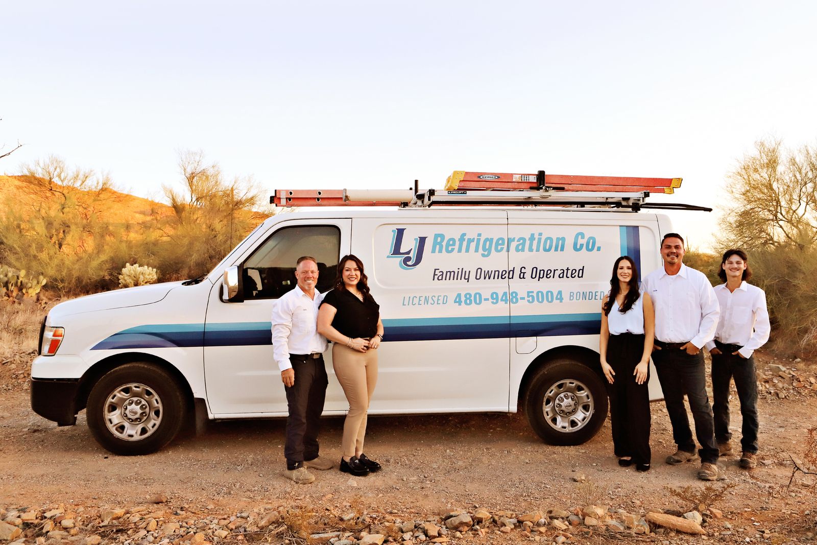 The LJ Refrigeration family team standing with their lettered service van in the Sonoran Desert at golden hour